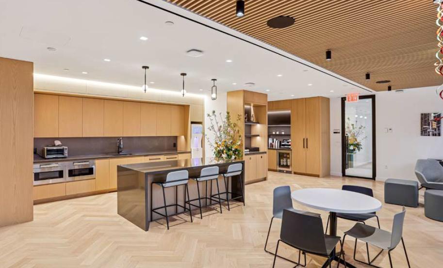 Modern office kitchen with island, seating, wood cabinetry, and lounge space